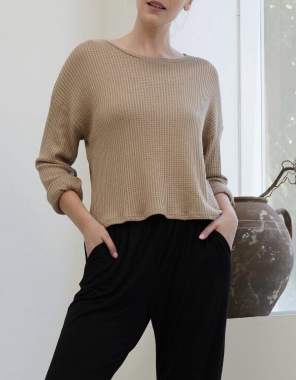 A woman wearing black pants and beige sweater.